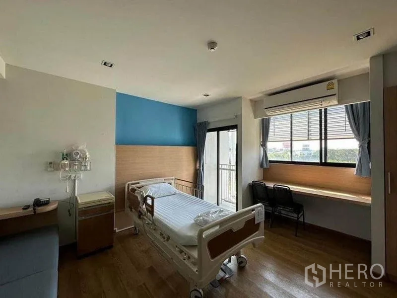 独立商业地产 出租在Bang Kapi, Bangkok - 私密病房式空间，配病床、蓝色点缀墙、大窗、嵌入式书桌与空调。