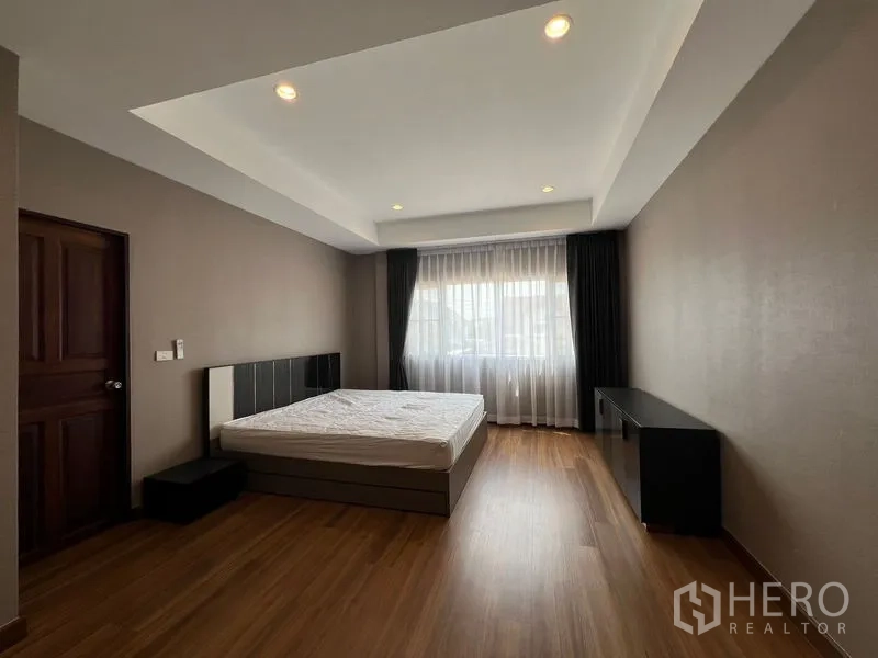 Detached House for sale in Mueang Pathum Thani, Pathum Thani - Sunlit second bedroom with bed, cove ceiling and a wide curtained window.