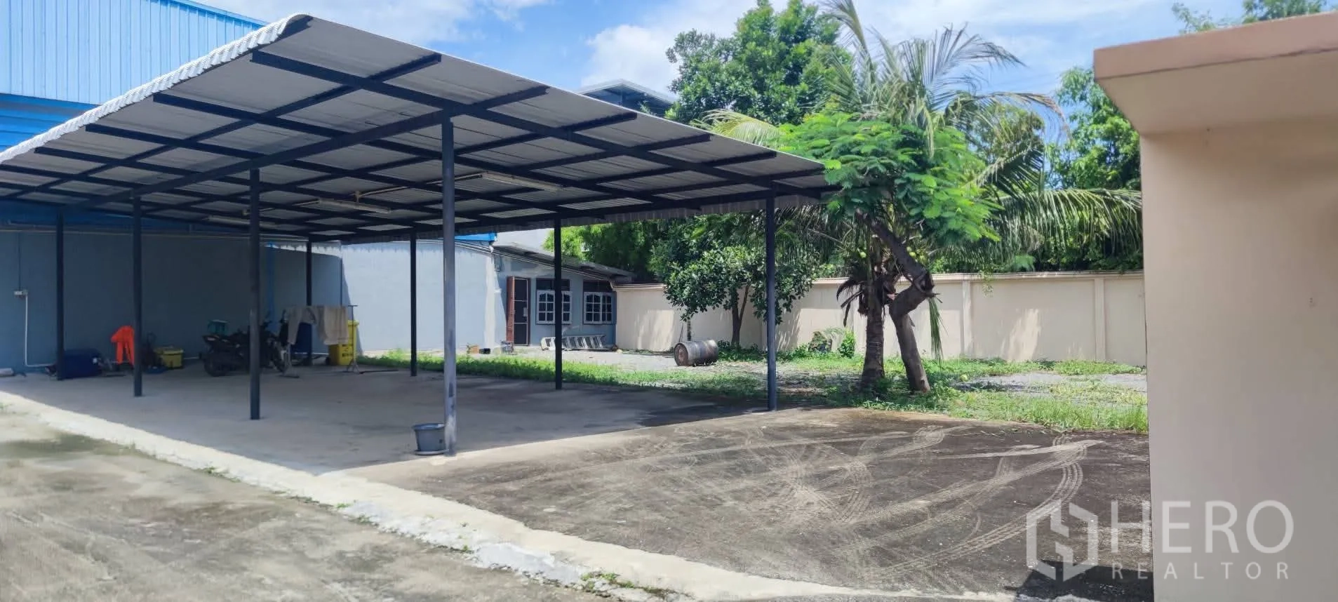 Warehouse for sale in Thung Khru, Bangkok - Large metal-roof carport with open yard and trees.