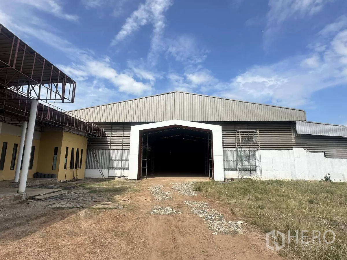Warehouse for sale in Nong Chok, Bangkok - Front exterior of a large steel-clad warehouse with wide entrance and open yard under blue sky in Nong Chok, Bangkok.