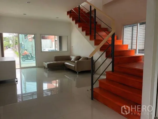 Shophouse for sale in Bueng Kum, Bangkok - Bright ground-floor space with glossy tiles, an L-shaped sofa and a wooden staircase in a shophouse.