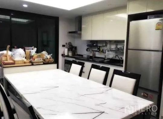 Townhouse for rent in Bang Rak, Bangkok - Modern kitchen and dining area with a marble-top table, built-in cabinets, and stainless-steel fridge.