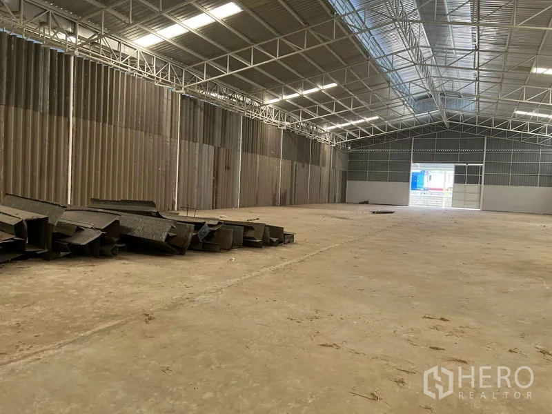 Warehouse for rent in Min Buri, Bangkok - Large warehouse bay with open loading door and stacked steel sections on the floor.