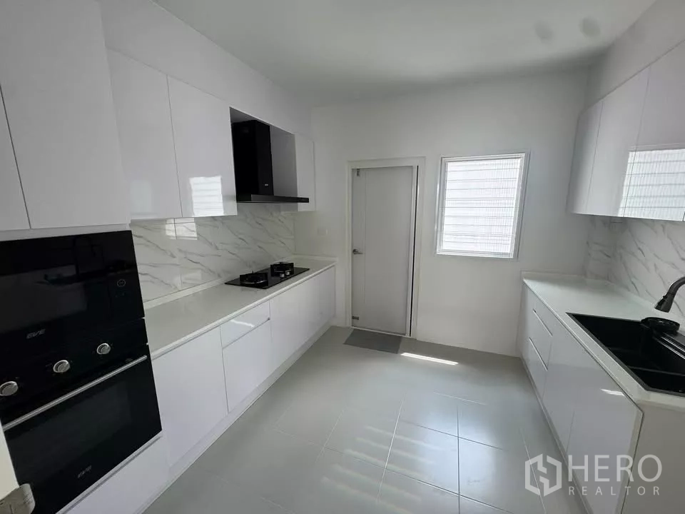 Detached House for rent or sale in Bang Bo, Samut Prakan - Sleek white built-in kitchen with marble backsplash, gas hob, and wall ovens.