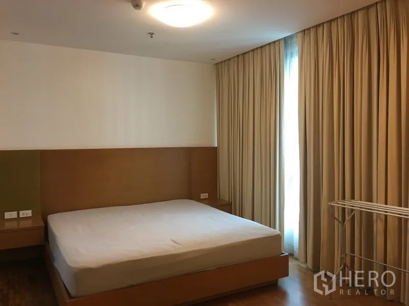 Condominium for rent in Pathum Wan, Bangkok - Spacious master bedroom with king bed, floor-to-ceiling curtains, warm lighting and wood flooring.