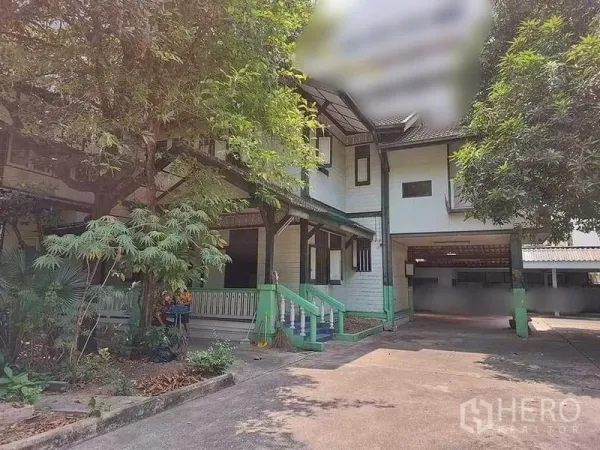 Detached House for rent in Bang Rak, Bangkok - Front exterior of two-storey wooden house with driveway, porch, trees, and covered carport.