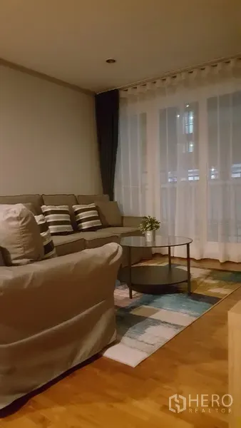 คอนโด ให้เช่าในWatthana, Bangkok - มุมห้องนั่งเล่นยามค่ำ พร้อมม่านโปร่งเต็มบานและโซฟาสีเทา