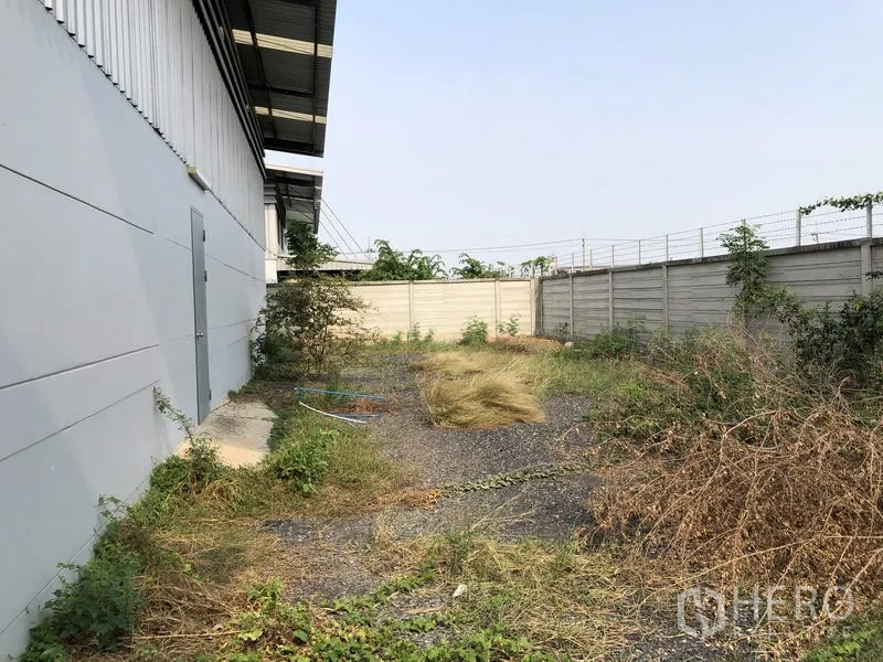 货栈 出租或出售在Lam Luk Ka, Pathum Thani - 建筑侧院带碎石与绿植，周边为混凝土围墙。