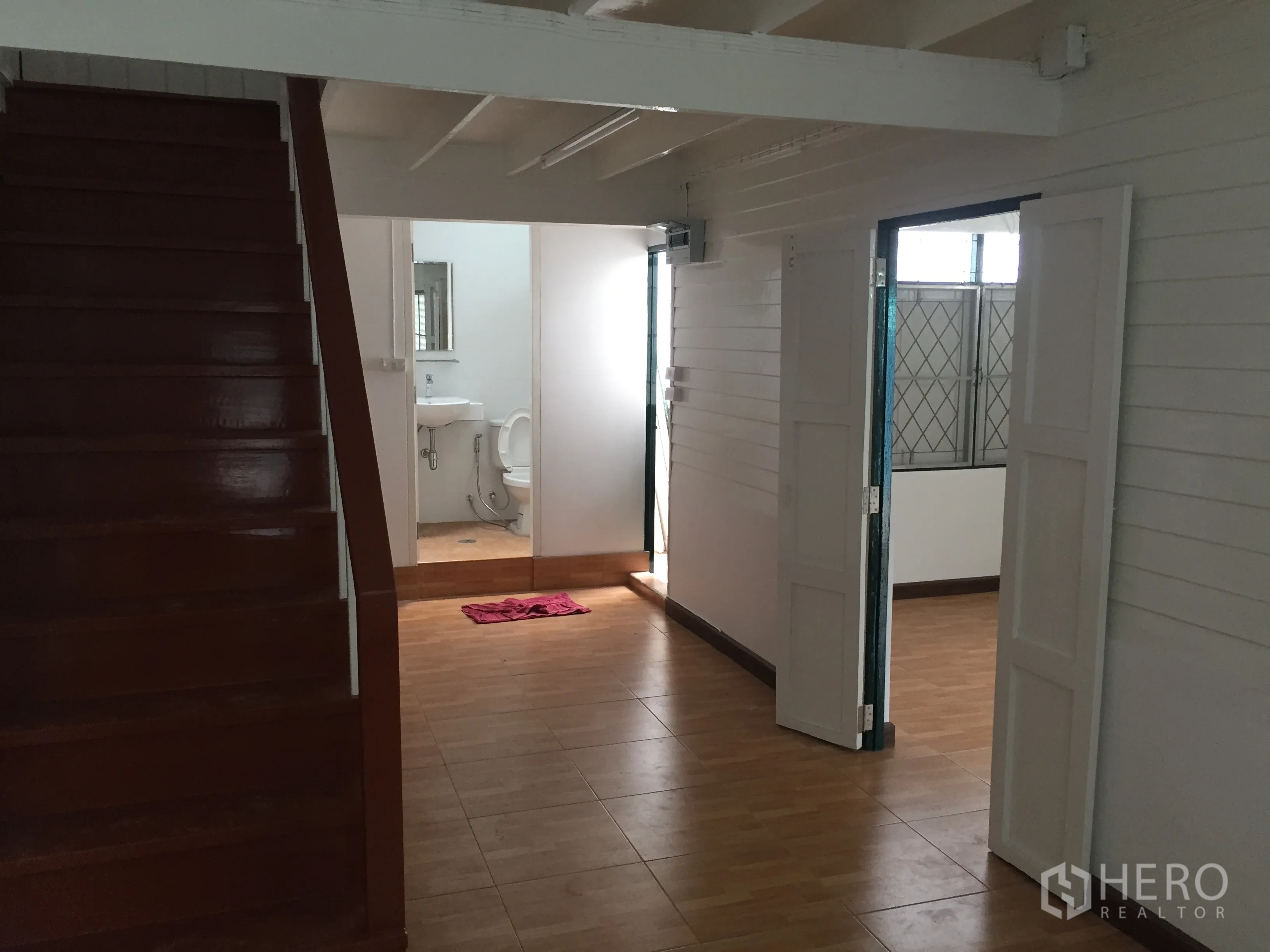 Detached House for rent in Bang Rak, Bangkok - Ground-floor corridor with polished wooden staircase, bathroom entrance, and white double doors.