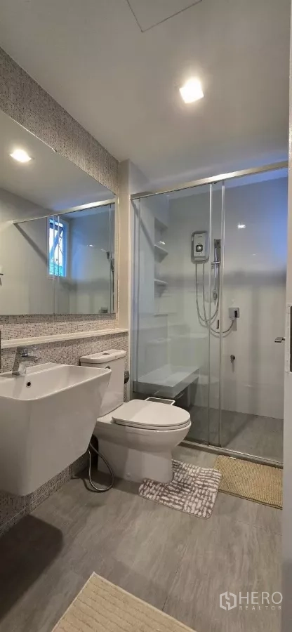 Detached House for rent in Samut Prakan - Bathroom with glass-enclosed shower, large mirror and modern fixtures.