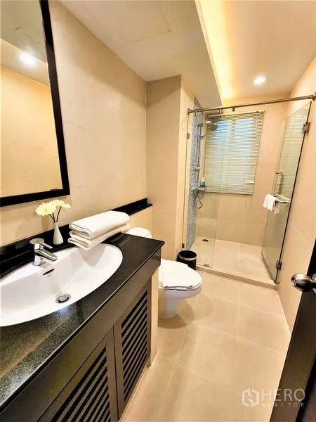 公寓 出租在Bang Rak, Bangkok - 现代卫浴，玻璃淋浴间、洗手台与米色瓷砖。