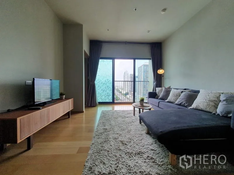 公寓 出租在Ratchathewi, Bangkok - 宽敞客厅，转角沙发、地毯和电视，朝向大窗。