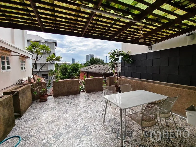 Townhouse for rent or sale in Bang Kho Laem, Bangkok - Covered terrace with dining table, potted trees and skyline view over the neighborhood.