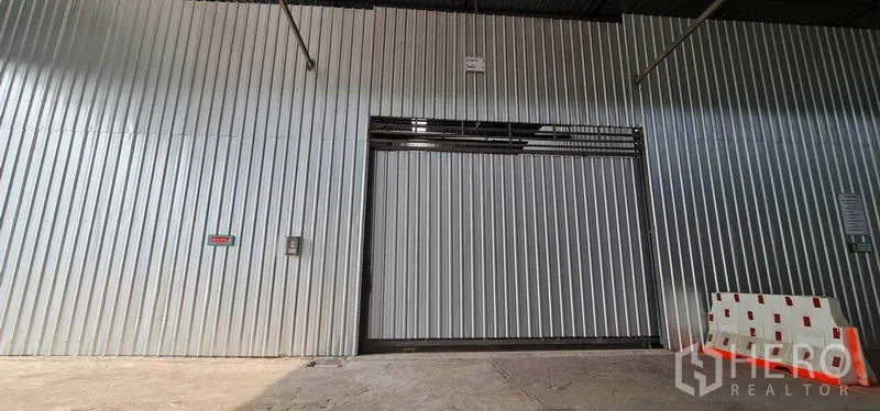 คลังสินค้า ให้เช่าในPak Kret, Nonthaburi - ประตูบานเลื่อนโลหะลูกฟูกขนาดใหญ่บริเวณทางเข้าโกดังพร้อมพื้นที่ขนถ่ายสินค้า