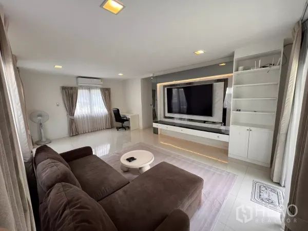 บ้าน ให้เช่าในLat Krabang, Bangkok - มุมนั่งเล่นพร้อมโซฟาตัวแอล ชั้นวางของ และผ้าม่านทึบสูงจรดพื้น