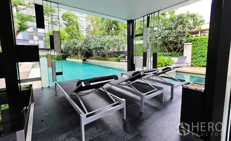 คอนโด ให้เช่าในWatthana, Bangkok - เก้าอี้อาบแดดใต้ร่มเงาข้างสระว่ายน้ำกลางแจ้งรายล้อมด้วยต้นไม้