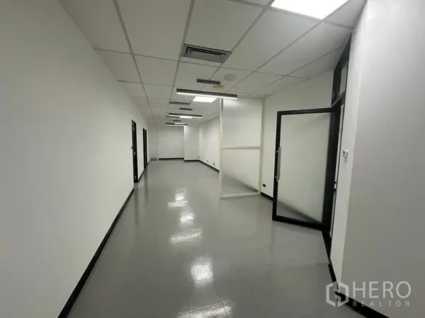 Office Space for rent - Long workspace corridor with ceiling lights, frosted glass partition and open doorway.