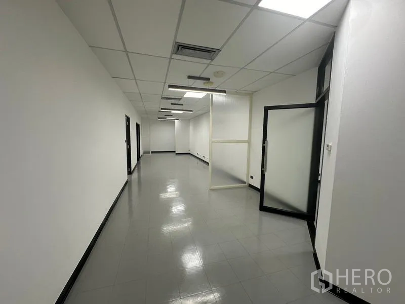 Office Space for rent - Long workspace corridor with ceiling lights, frosted glass partition and open doorway.