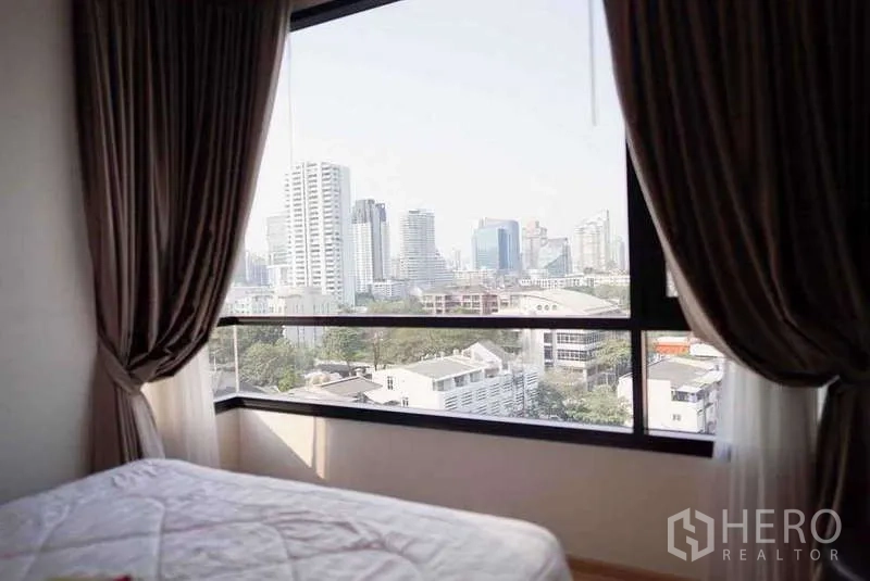 Condominium for rent or sale in Watthana, Bangkok - Bedroom window framing a Bangkok skyline view with dark drapes and abundant daylight.