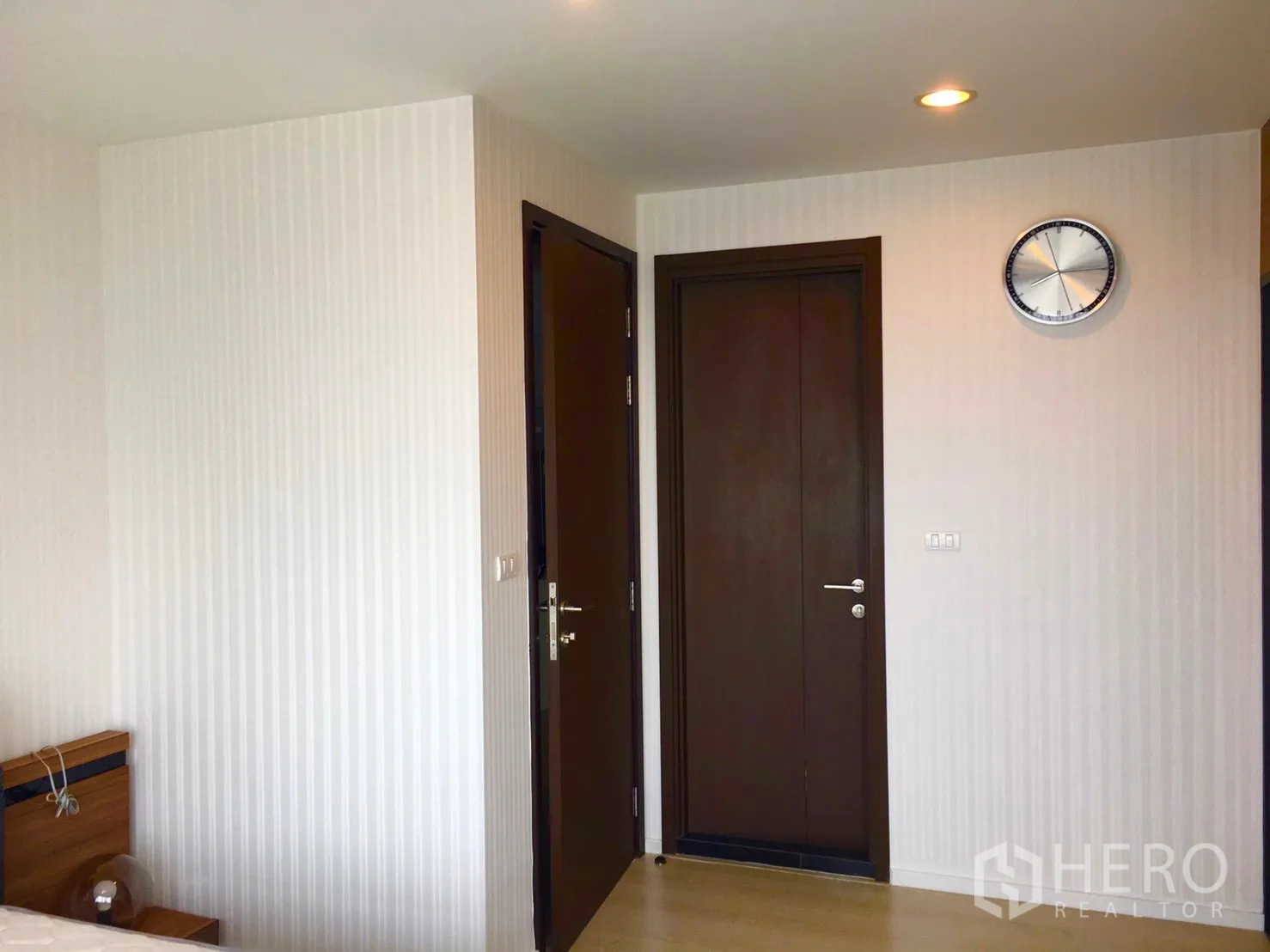 Condominium for sale in Sathon, Bangkok - Bedroom corridor with two wooden doors, wall clock and light wood flooring.