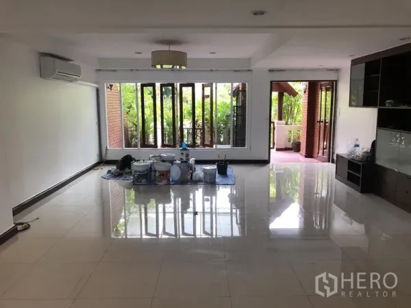 Townhouse for rent or sale in Watthana, Bangkok - Bright living room with glossy tile floors, wall-to-wall windows and access to a covered terrace.