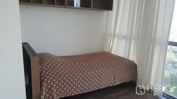 คอนโด ให้เช่าในBangkok - ห้องนอนขนาดกะทัดรัด มีเตียงเดี่ยว ผ้าม่านโปร่ง และหน้าต่างเต็มบานมองวิวเมือง