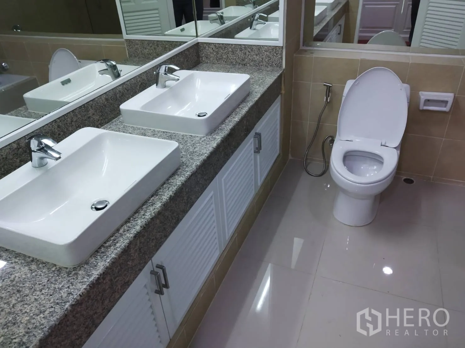 Condominium for rent in Pathum Wan, Bangkok - Bathroom with double square basins on a granite countertop, large mirror and toilet.