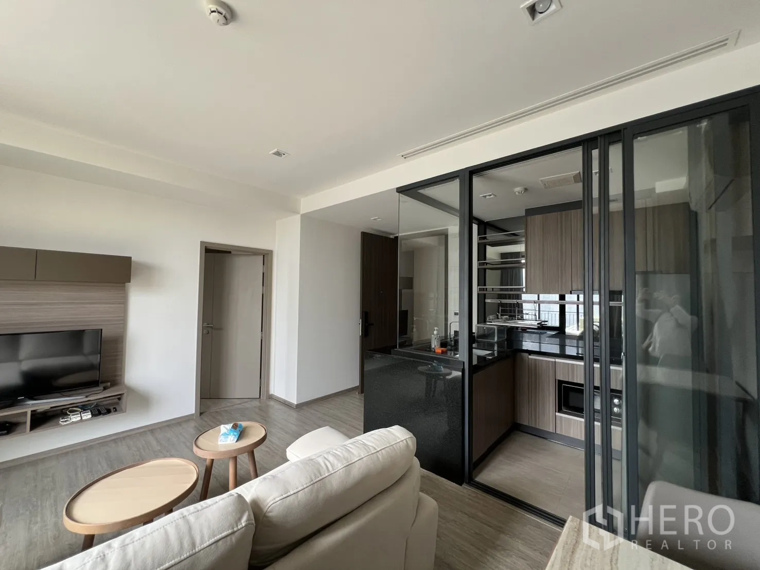 公寓 for rent in Watthana, Bangkok - 客厅设壁挂电视柜、沙发与通往玻璃隔断厨房的入口。