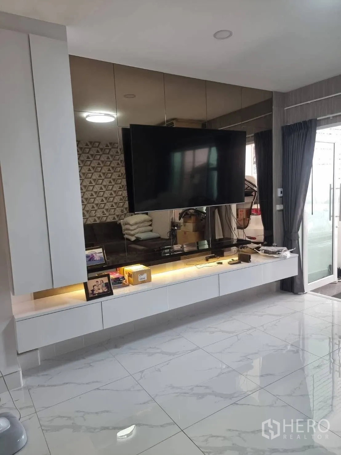 Townhouse for rent in Din Daeng, Bangkok - Living area with floating TV console, glossy marble-look floor and mirror wall.