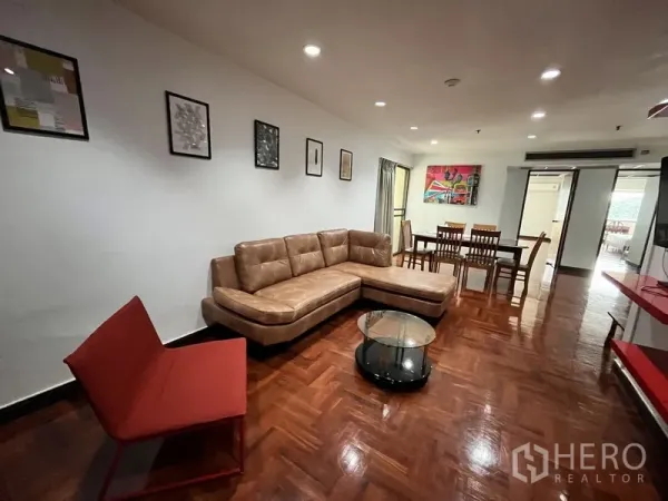 Condominium for rent in Watthana, Bangkok - Bright living room with L-shaped leather sofa, red accent chair, glass coffee table and parquet floors.