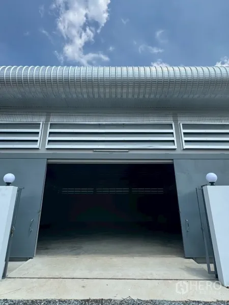 Warehouse for rent or sale in Nong Chok, Bangkok - Front view of warehouse with wide sliding steel door open and concrete driveway for easy truck access.