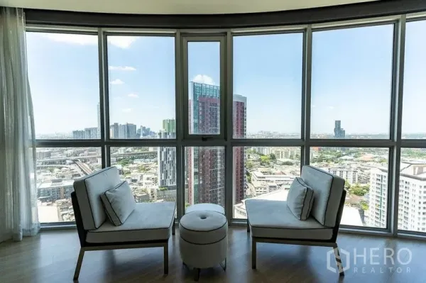 Condominium for rent - Curved floor-to-ceiling windows with two lounge chairs framing a wide Bangkok skyline view.