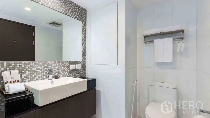 Apartment for rent in Watthana, Bangkok - Vanity with large mirror, sink and toilet in a bright tiled bathroom.