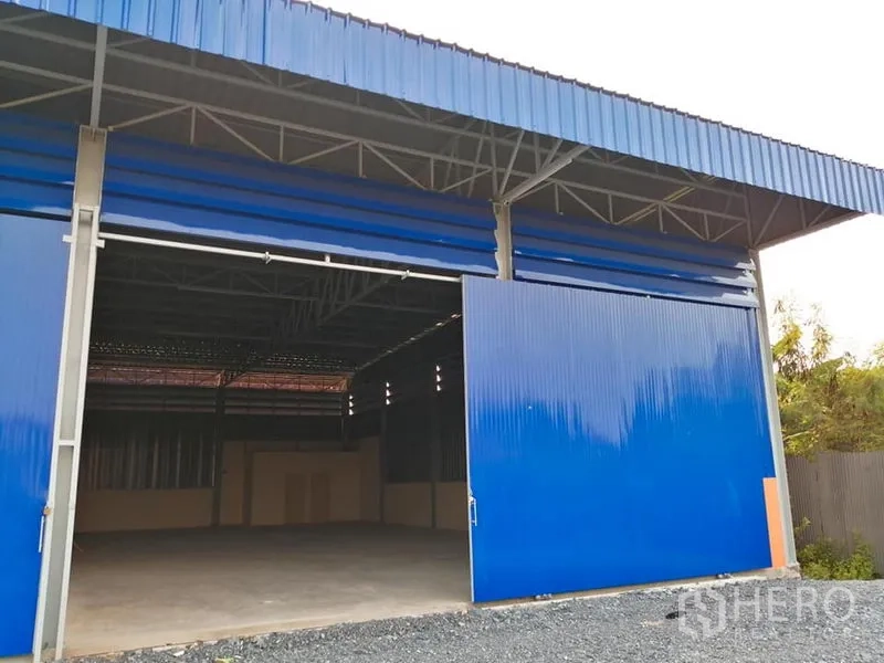 Warehouse for rent in Phra Samut Chedi, Samut Prakan - Blue steel warehouse facade with wide sliding doors and a gravel loading driveway.