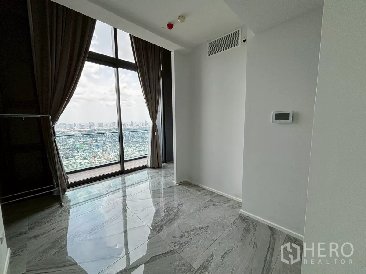 Condominium for sale in Bang Kho Laem, Bangkok - High-floor living area with floor-to-ceiling windows, grey marble tiles and west-facing city skyline view with curtains.