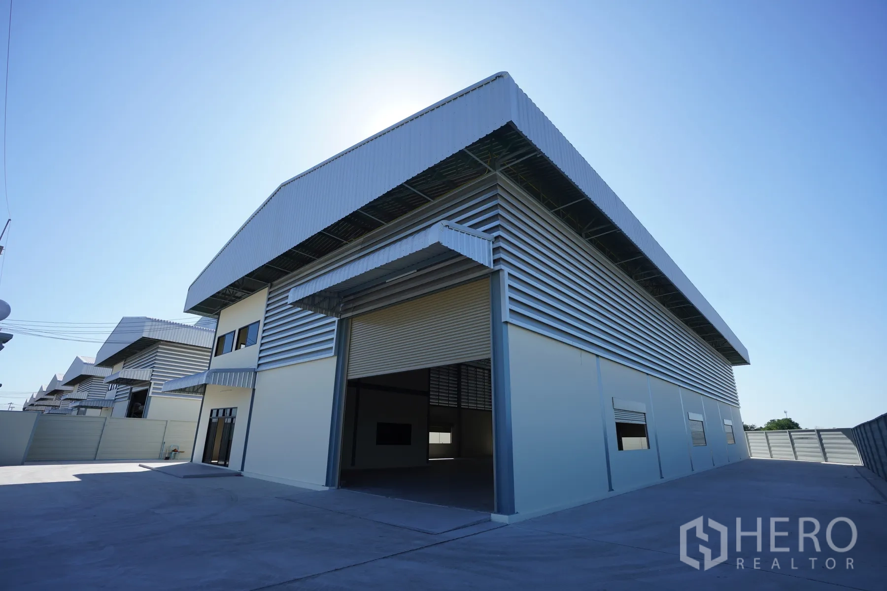 Factory for rent in Mueang Samut Prakan, Samut Prakan - Modern factory exterior featuring a wide roller shutter and broad concrete driveway.