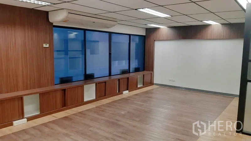 Office Space for rent in Chatuchak, Bangkok - Built-in wooden storage beneath blue-tinted windows with an air conditioner and white feature wall.