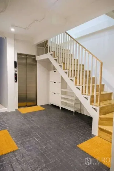 Home Office for rent in Phra Khanong, Bangkok - Ground-floor lobby with dark tile flooring, wooden staircase, white storage and a stainless passenger lift.