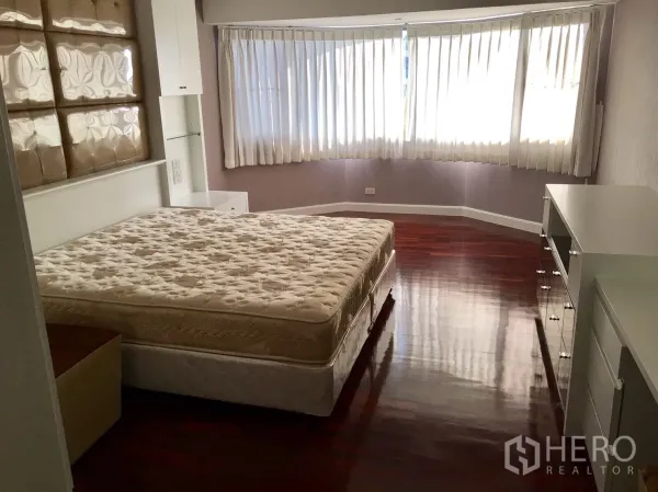 Condominium for rent in Watthana, Bangkok - Spacious bedroom with curved bay window, white curtains and glossy wooden floors in a Watthana condominium.