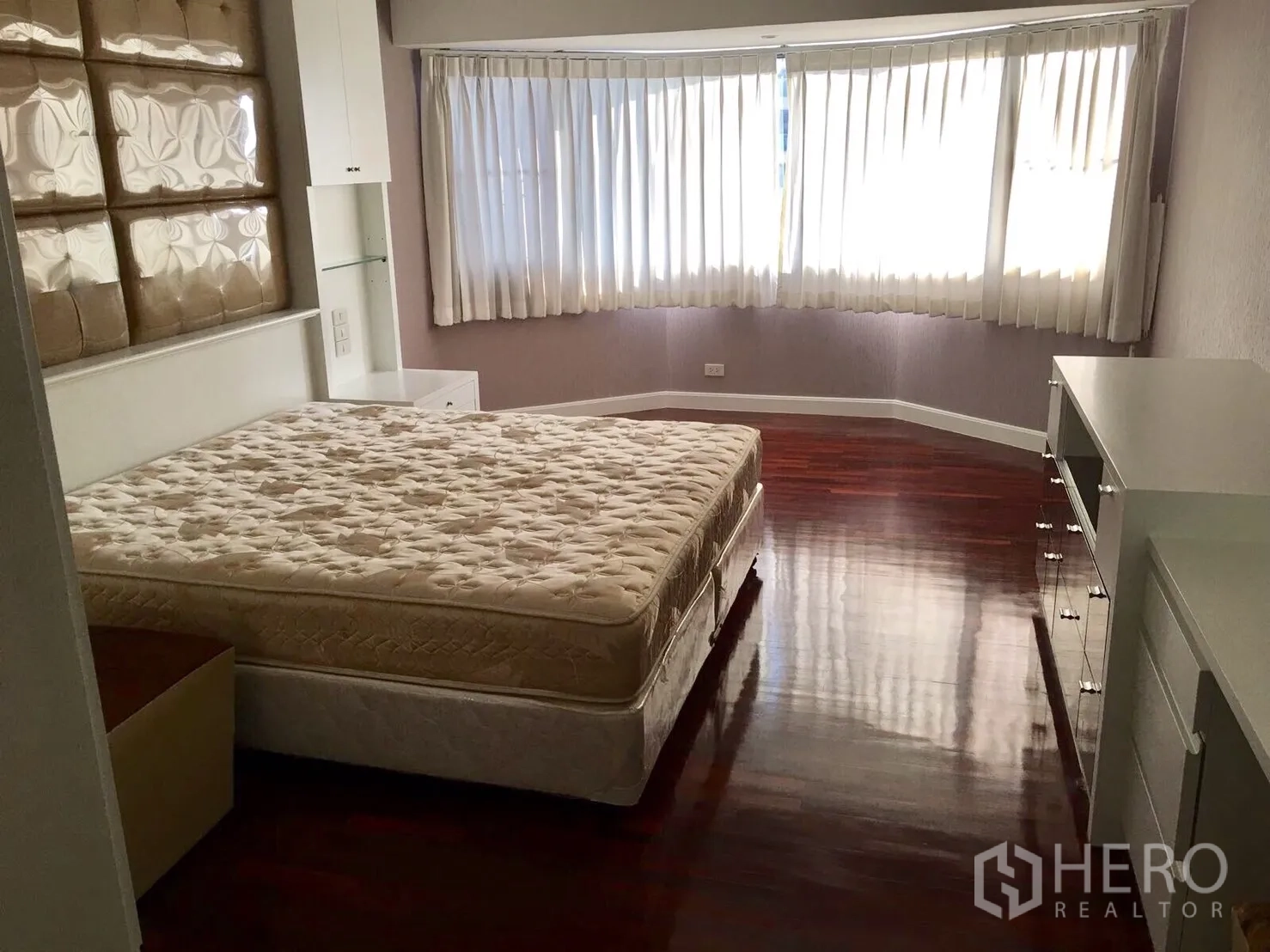 Condominium for rent in Watthana, Bangkok - Spacious bedroom with curved bay window, white curtains and glossy wooden floors in a Watthana condominium.