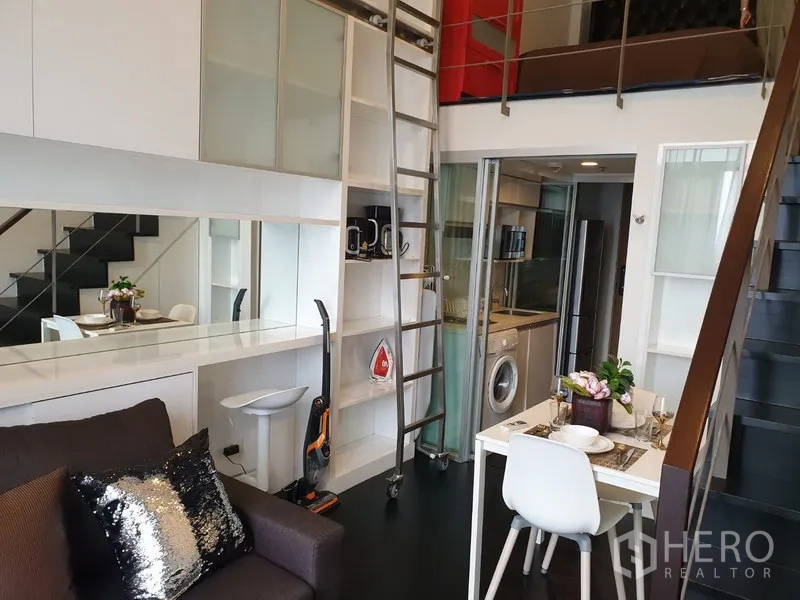 公寓 出租在Khlong Toei, Bangkok - 阁楼风客厅，带内置收纳与移动梯子，玻璃隔断小厨房和小型餐桌。