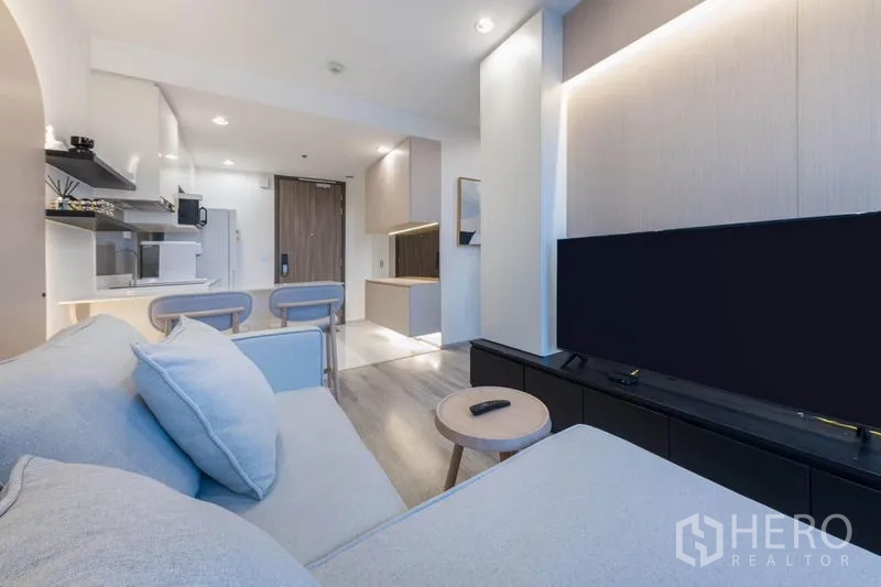 Condominium for rent in Bang Na, Bangkok - Living area view from the sofa showing a long TV console and open plan to the kitchen.