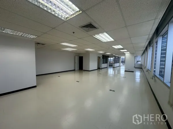 สำนักงาน ให้เช่า - พื้นที่สำนักงานแบบเปิดโล่ง ฝ้าเพดานหลุม ไฟฟลูออเรสเซนต์ และหน้าต่างบานใหญ่เรียงยาว มีห้องกั้นกระจกด้านในสุด