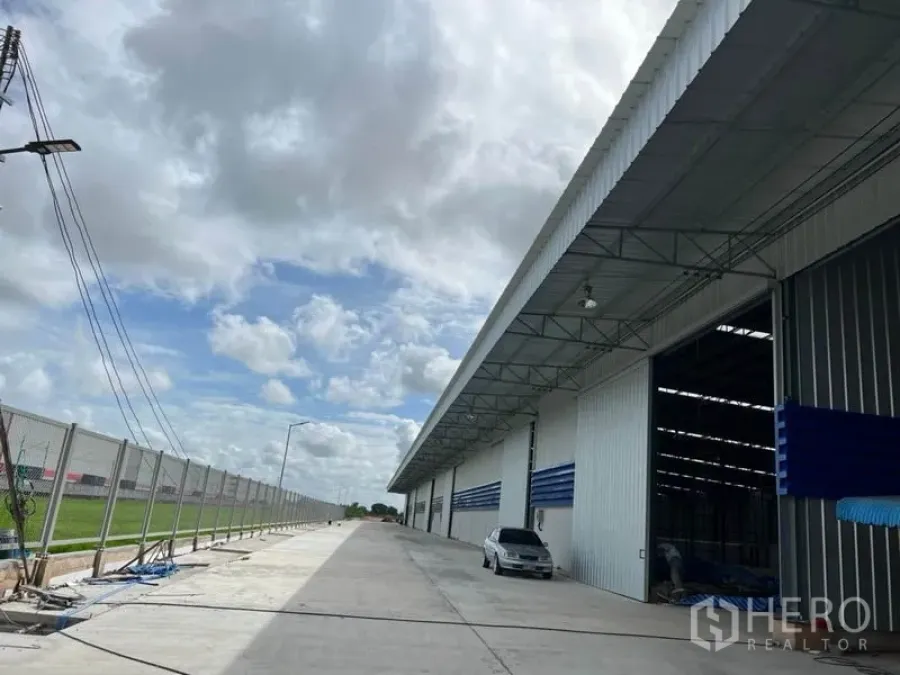 Warehouse for rent in Lat Krabang, Bangkok - Modern warehouse exterior in Lat Krabang with a wide concrete driveway, loading bays, and security fencing under a cloudy sky.