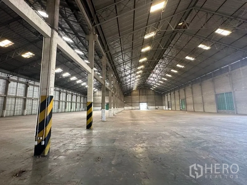 货栈 出租在Mueang Pathum Thani, Pathum Thani - 开放式仓储区，混凝土柱带黄色安全标识，地坪开阔。