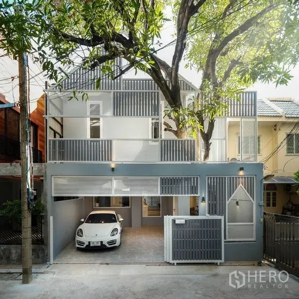 联排别墅 出租在Watthana, Bangkok - 现代联排外立面，灰色调，阳台、滑动大门与带树荫的车库。