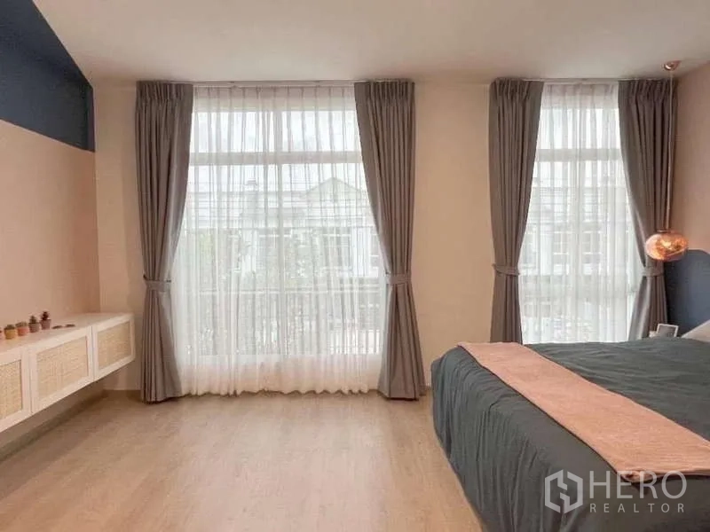 Townhouse for rent in Bang Bo, Samut Prakan - Bedroom space with floor-to-ceiling windows, sheer curtains and a floating cabinet.