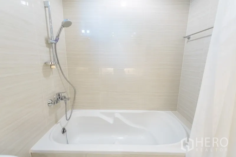 房间 出租在Yan Nawa, Bangkok - 浅色瓷砖墙面的浴室，设浴缸与手持花洒。
