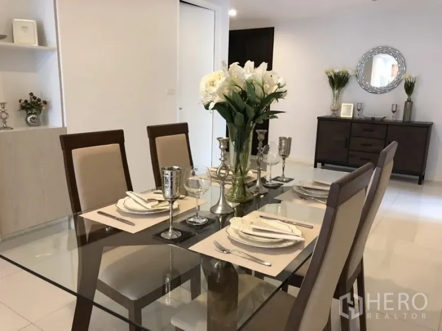 Condominium for rent in Watthana, Bangkok - Elegant dining table setting with flowers and silverware, sideboard and round mirror in a bright room.