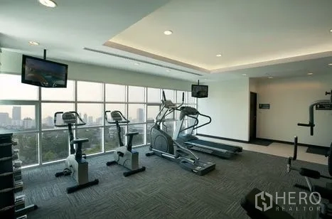 Condominium for rent or sale in Khlong Toei, Bangkok - Fitness center with treadmills, elliptical, bikes, free weights, and city views through large windows.